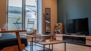 Moderni olohuone, jossa on sohva, sohvapöytä, televisio ja suuret ikkunat, joista on näkymä ulos.