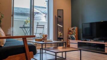 A modern living room with a sofa, coffee table, TV, and a view through large windows.