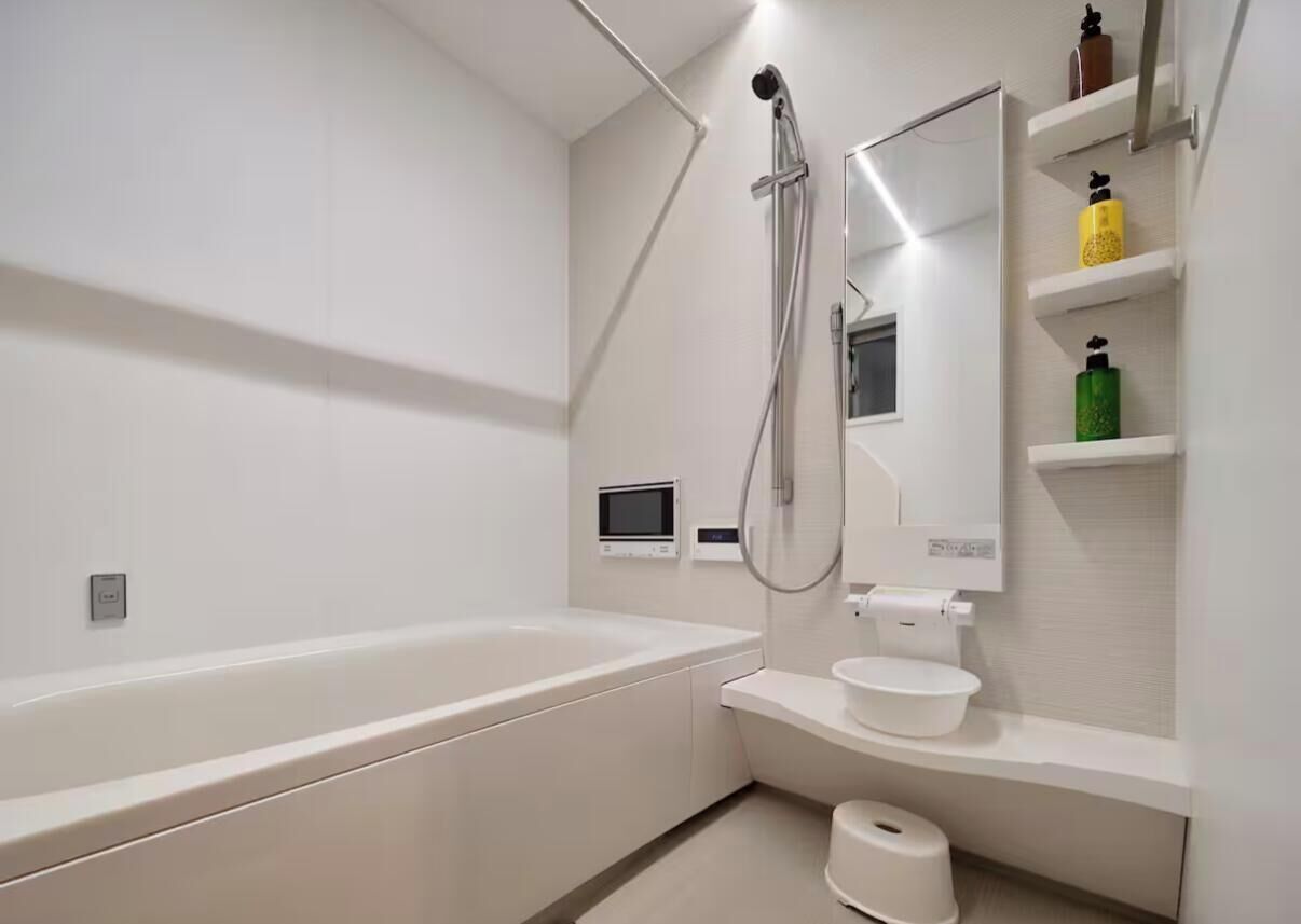 Casa de banho moderna com banheira, sanita e chuveiro. Há prateleiras com artigos de higiene pessoal.