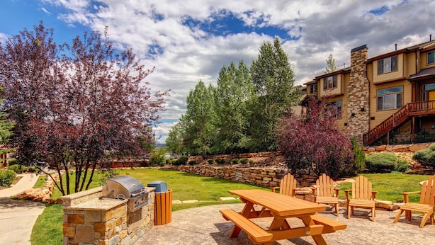 Un'area patio con una griglia barbecue, tavolo da picnic e poltrone Adirondack.