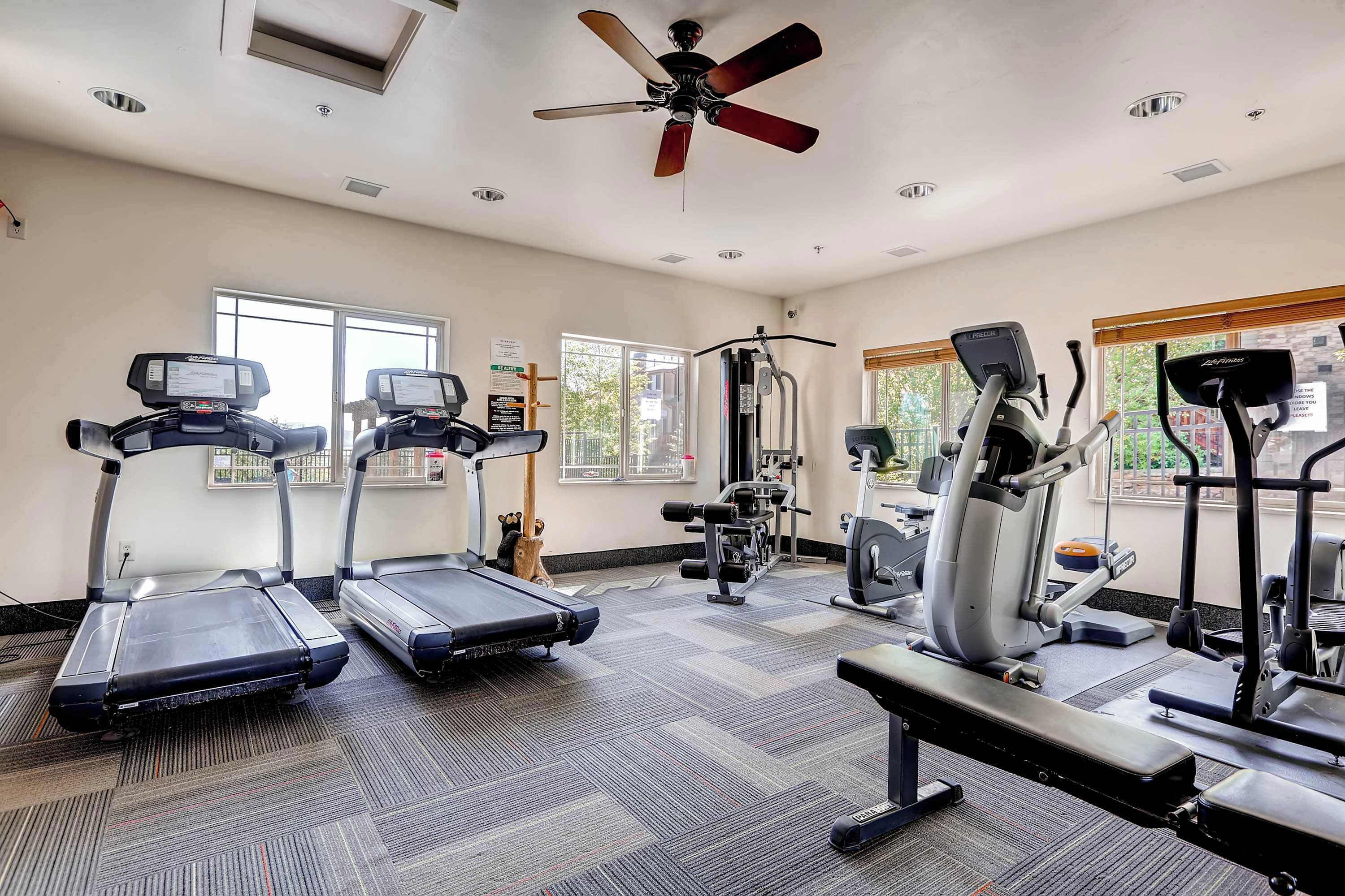 A gym with treadmills, elliptical machines, and a ceiling fan.