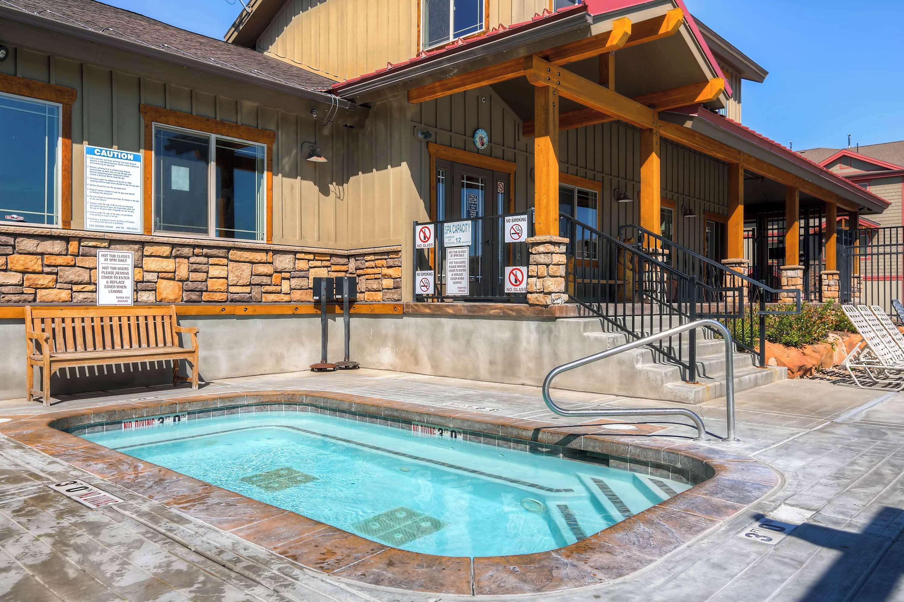 A pool area with a stone wall, wooden bench, and a building with a red roof and wooden beams.