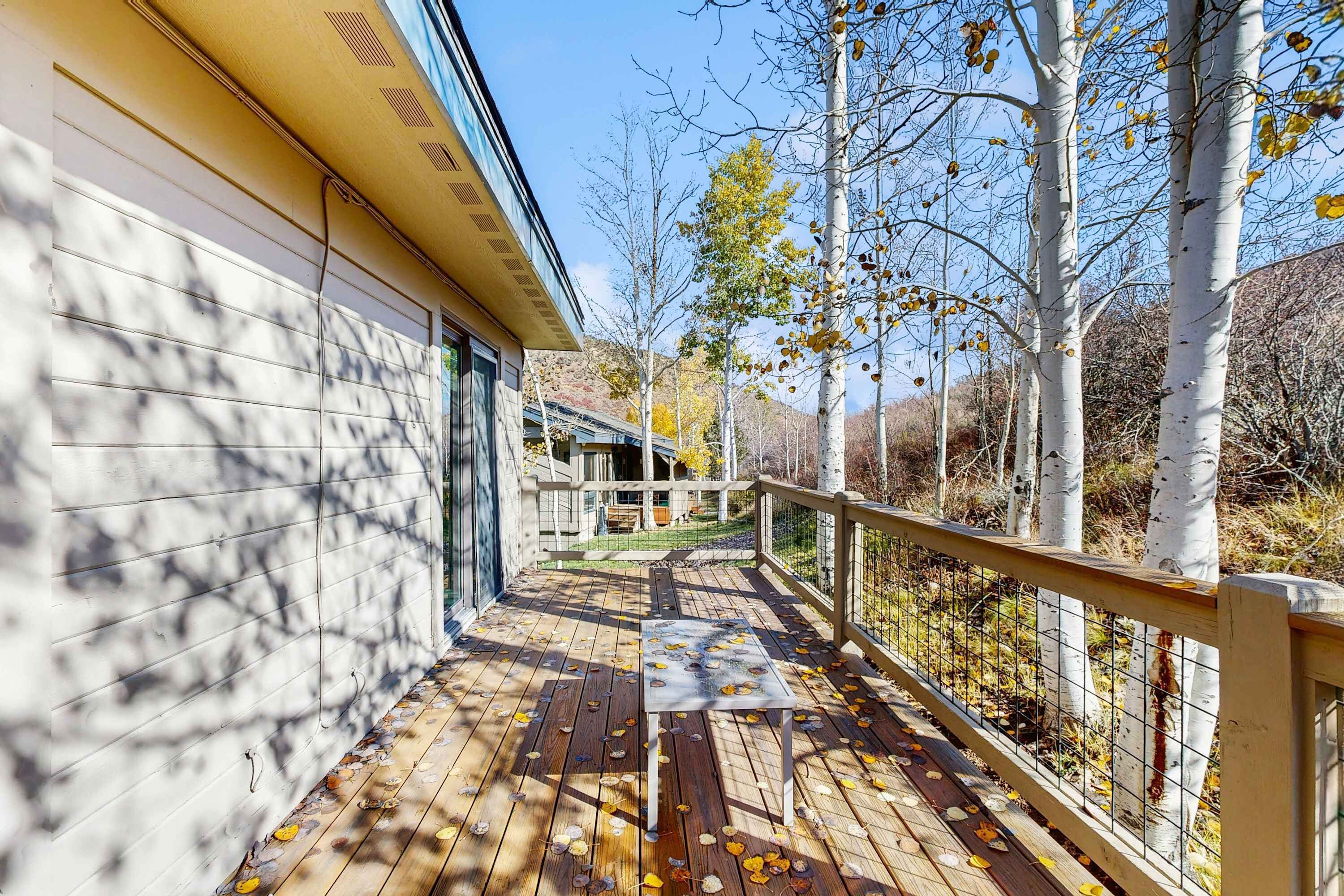 A wooden deck with a table, a railing, and trees with autumn leaves.