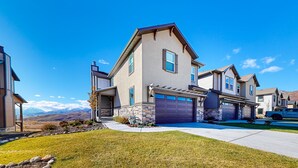 A two-story house with a garage, a stone foundation, and a clear view of mountains in the background. - Stunning townhome with  unobstructed views, amenities for the health conscious (Heber City)