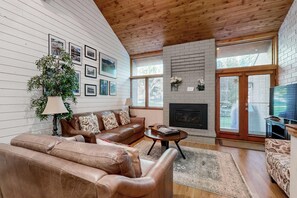 A living room with a fireplace, leather sofas, a coffee table, and a large window. - All-Season Escape - Heated Pool , Hot Tub, Pickle B - Stroll to Lifts (Park City)