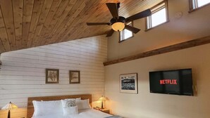 Ein Schlafzimmer mit einem Bett, einem Deckenventilator, einem Fernseher und gerahmten Bildern an der Wand.