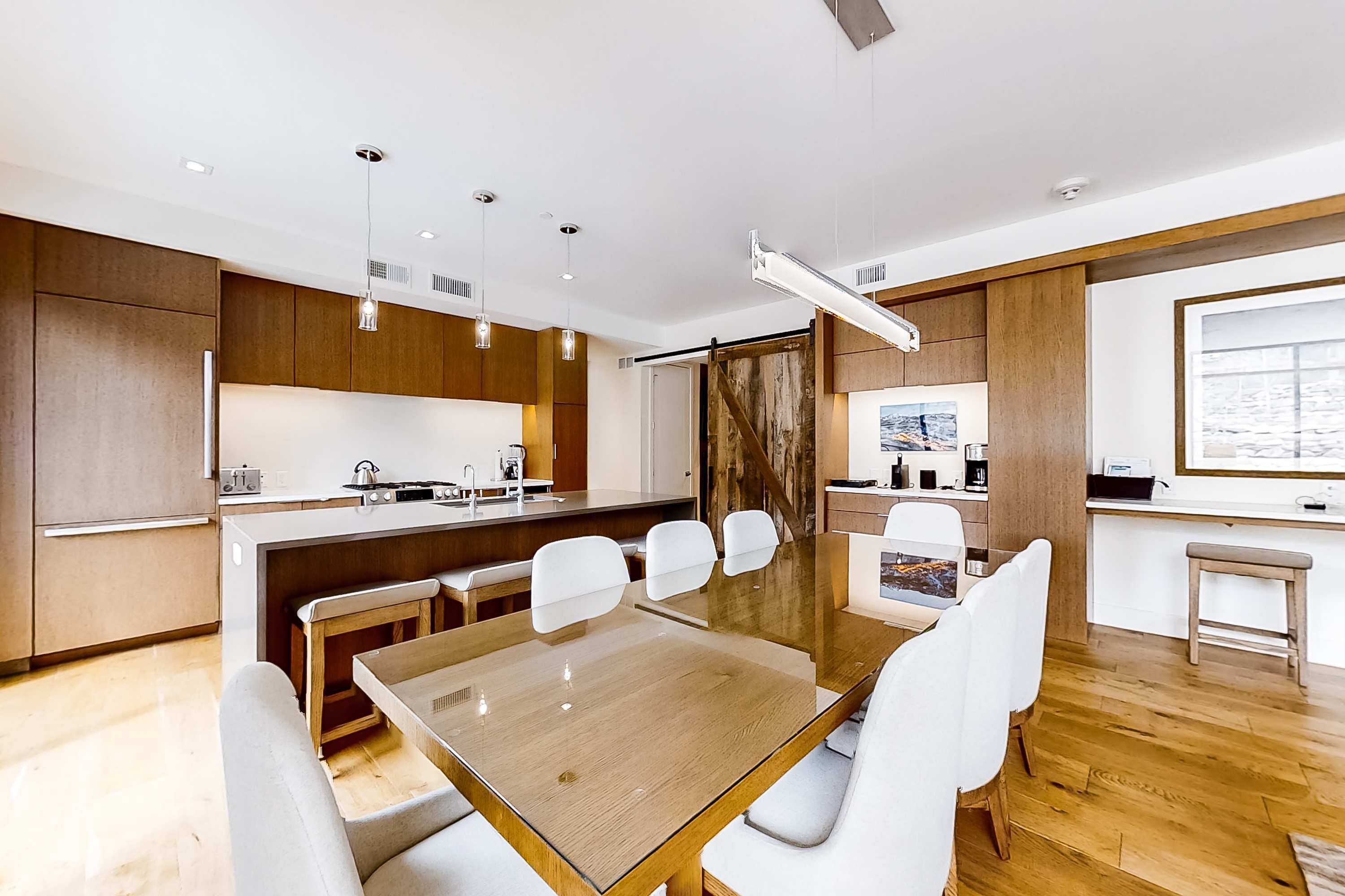 Une cuisine moderne avec un îlot central, des chaises blanches et une table à manger en bois.