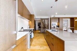 A modern kitchen with wooden cabinets, a central island, and a view into the living area. - All-Suite Ski-In, Ski-Out Penthouse - Pool, Hot Tub & Mountain-View Balcony (Park City)