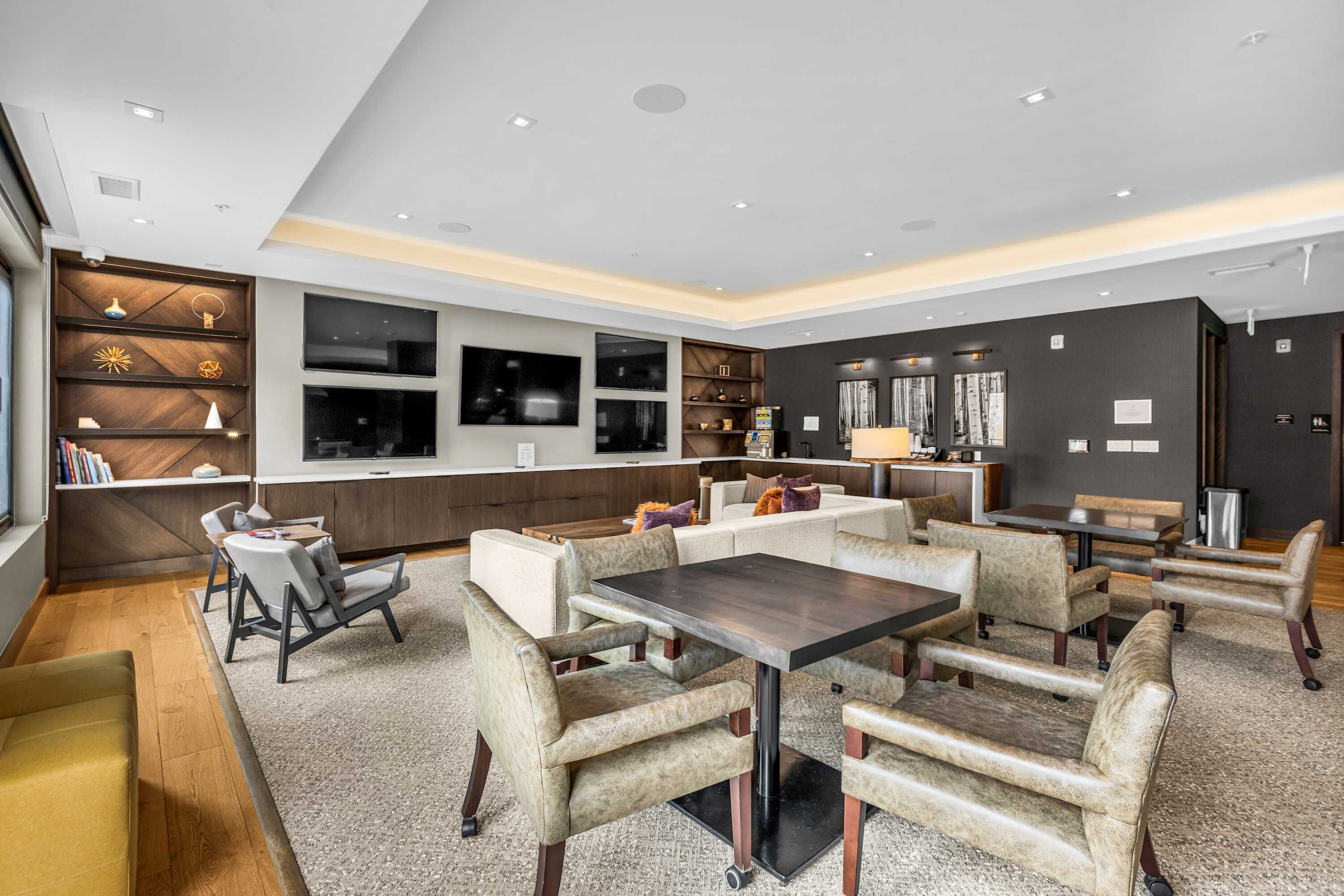 A modern hotel lobby with a central seating area, a bar, and a television mounted on the wall.