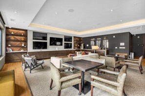 Un hall d’hôtel moderne avec un espace salon central, un bar et un téléviseur fixé au mur.