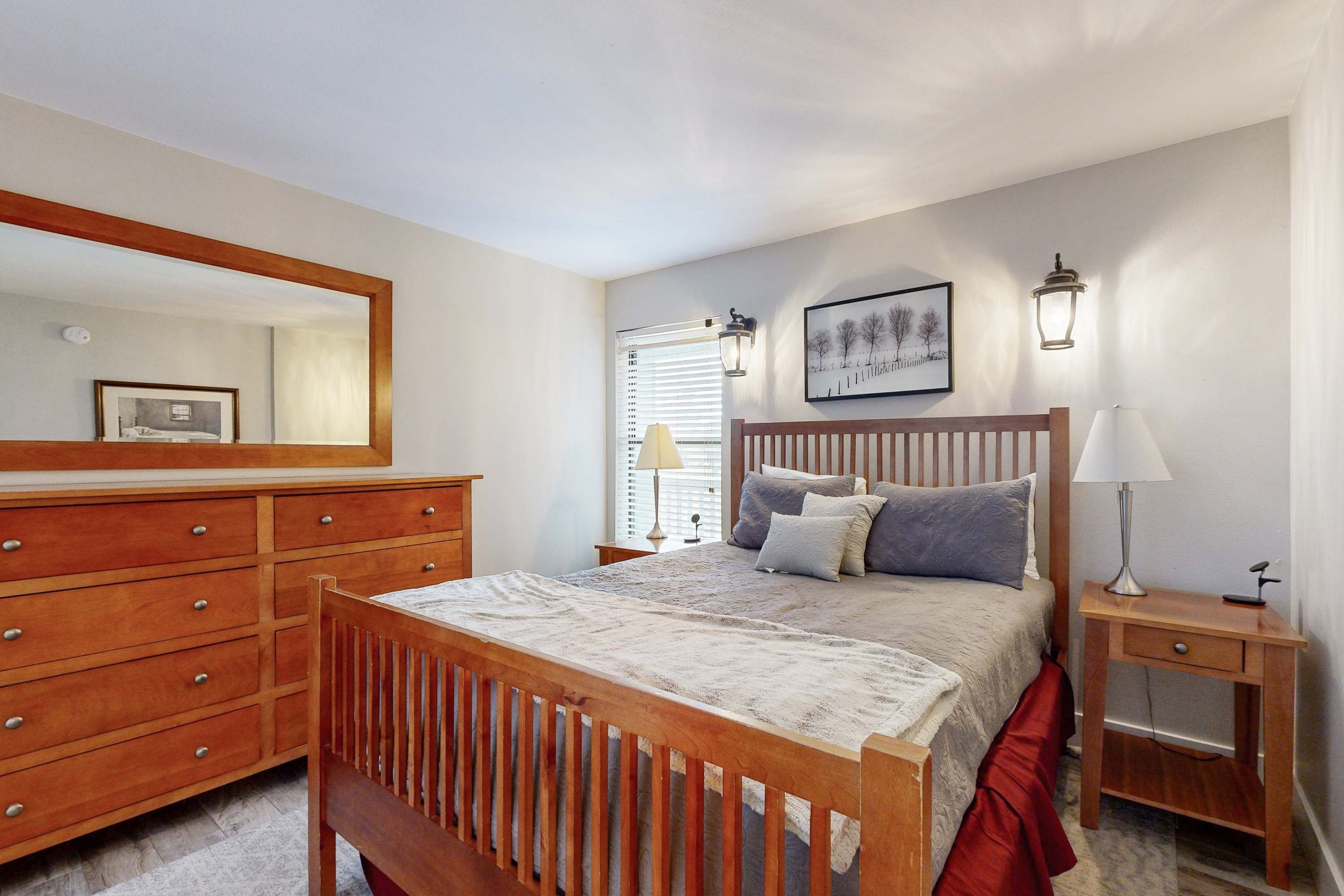 A bedroom with a wooden bed, a dresser, a nightstand, and a wall-mounted lamp.