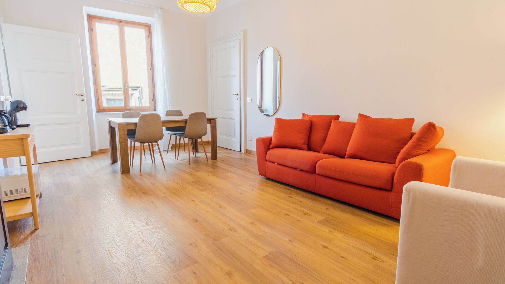 A room with a wooden floor, a dining table with chairs, a sofa, and a mirror.
