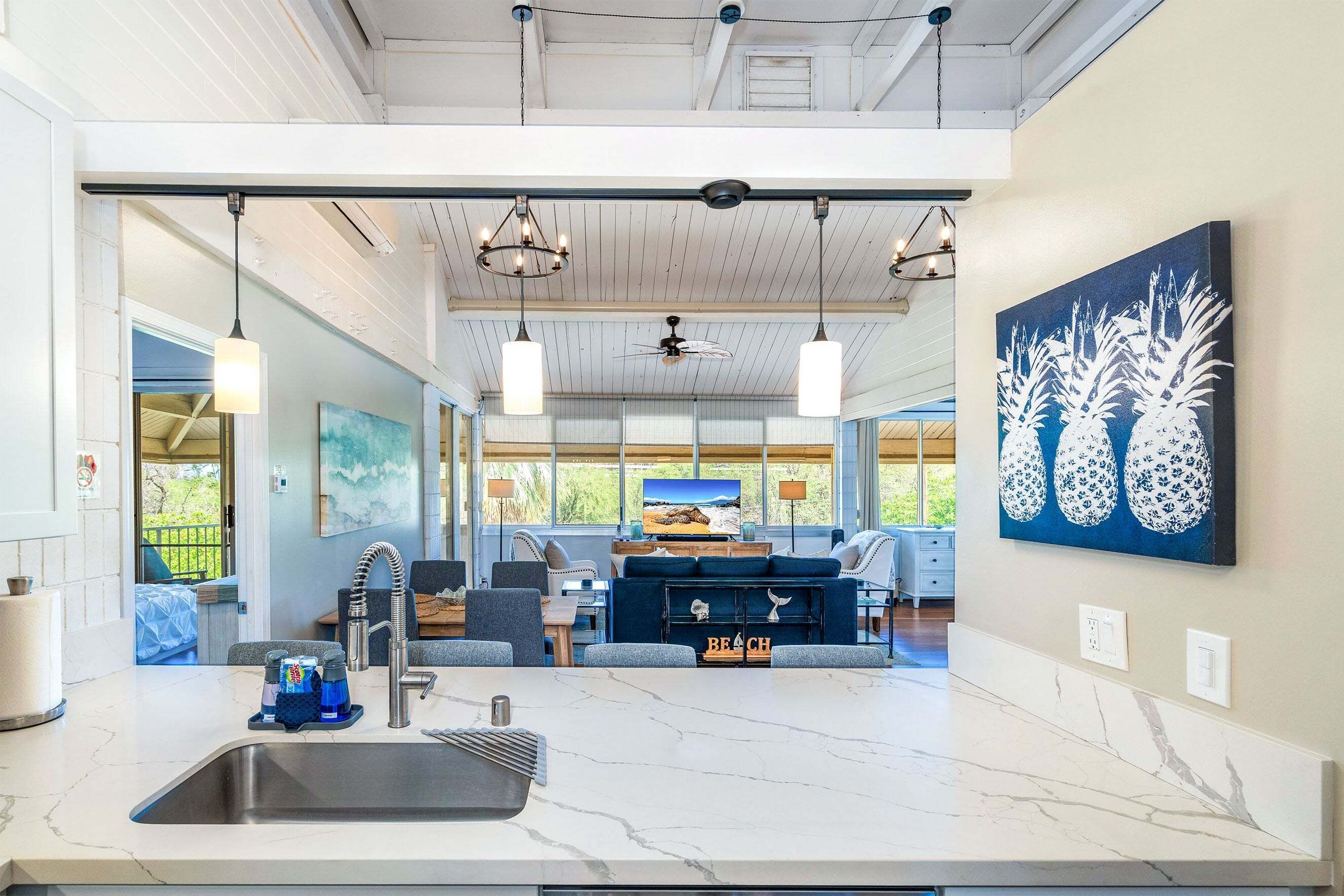 A modern kitchen with a marble countertop, a sink, and a dining area with a blue sofa and a television.