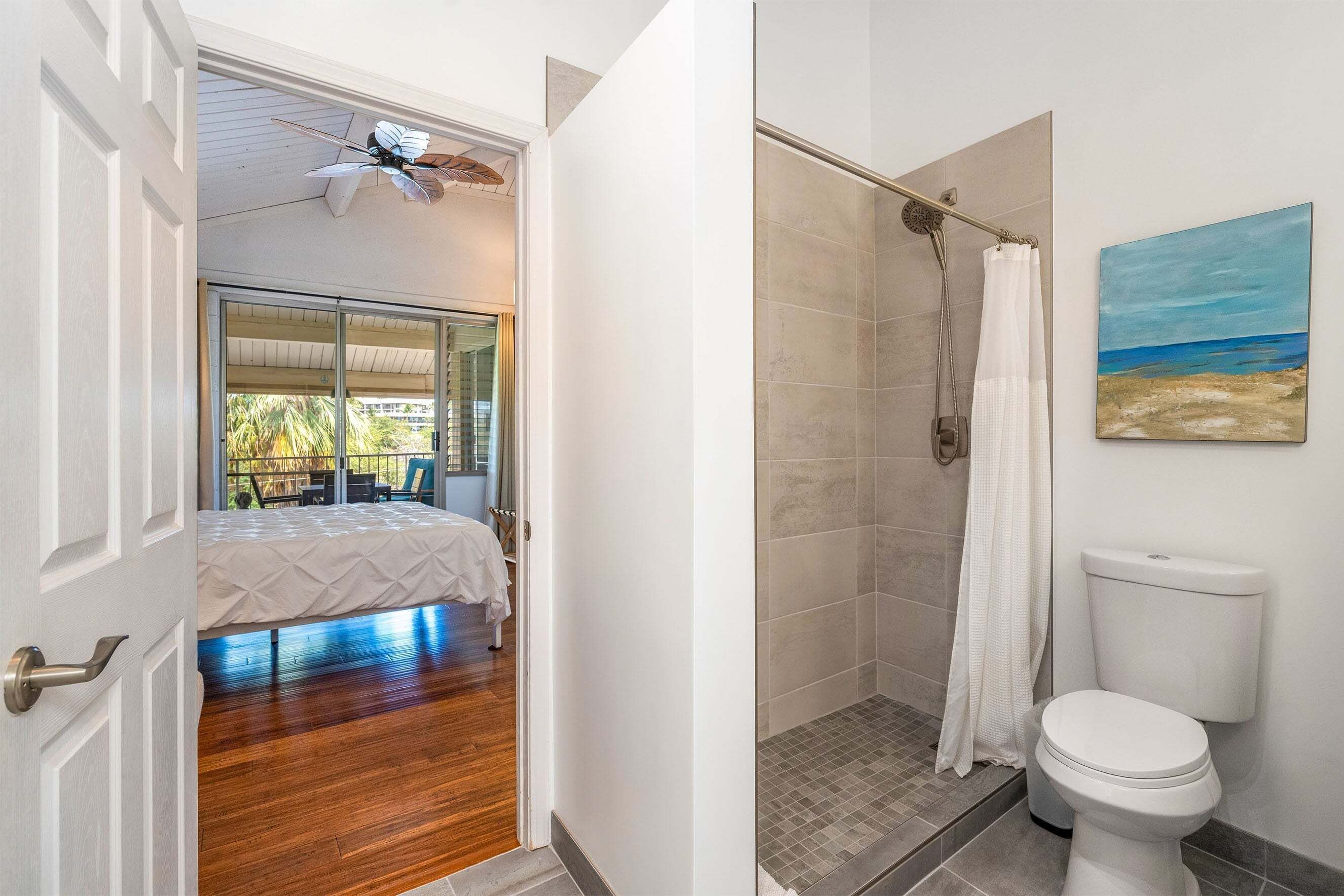 Un baño con ducha, inodoro y un cuadro de una playa.