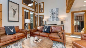 A spacious living room with leather sofas, a round wooden coffee table, and artwork on the walls. - Spectacular Townhome with  a Private Hot Tub, Free WiFi, AC, & Three Fireplaces (Park City)