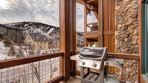 A balcony with a grill, stone wall, and a view of a snowy landscape. - Spectacular Townhome with  a Private Hot Tub, Free WiFi, AC, & Three Fireplaces (Park City)