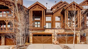 A multi-story wooden house with a stone facade, large garage doors, and a balcony. - Spectacular Townhome with  a Private Hot Tub, Free WiFi, AC, & Three Fireplaces (Park City)