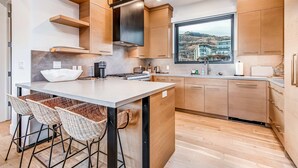 A modern kitchen with a central island, bar stools, wooden cabinets, and a view of a hillside. - Elegant townhome with mountain view, private hot tub, fireplace & lovely decor (Park City)