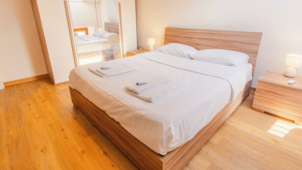 Ein Doppelbett mit Holz-Kopfteil, zwei Nachttische mit Lampen und ein großer Spiegel an der Wand.