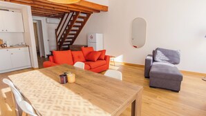 Ein gemütlicher Wohnbereich mit einem Holzesstisch, einem roten Sofa, einem grauen Sessel und einer Treppe, die in einen oberen Bereich führt.