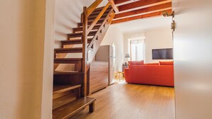 Eine Holztreppe führt zu einem Wohnbereich mit einem roten Sofa und einem Fernseher.