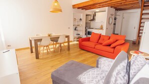 Ein modernes Wohnzimmer mit einem Holzesstisch, einer Couch und einer Küche im Hintergrund.