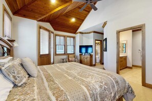 A bedroom with a large bed, wooden ceiling, a television, and a bathroom visible through an open door. - Home with Private Hot Tub, Mountain Views, & Resort Attractions (Park City)