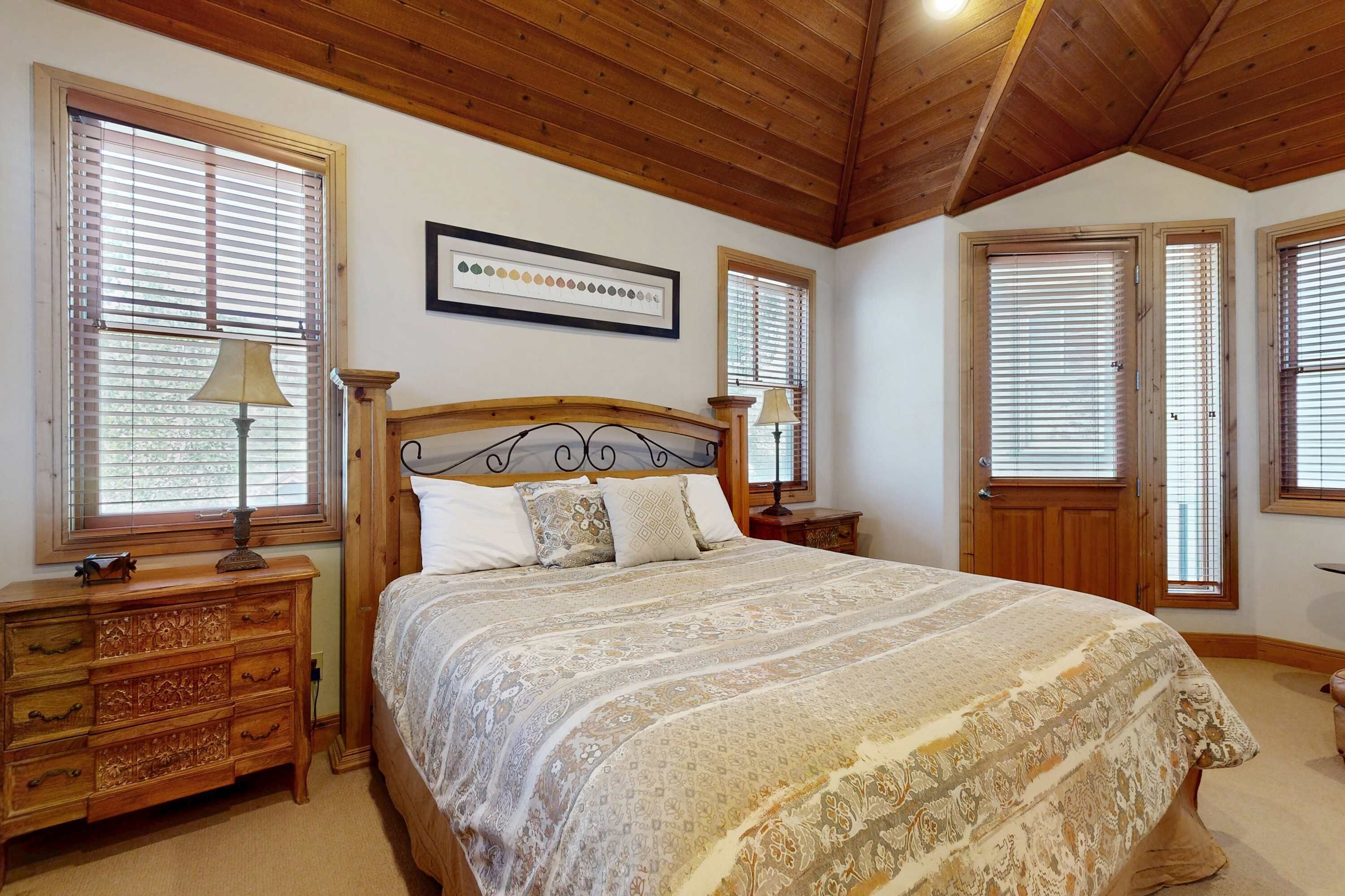 Un dormitorio con techo de madera, una cama con colcha estampada, un aparador de madera y un cuadro enmarcado en la pared.