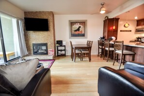 Een woonkamer met een open haard, een eetgedeelte met houten stoelen, een keuken met houten kastjes, en een flatscreen televisie aan de muur bevestigd.