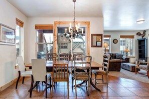 A dining area with a wooden table and chairs, a chandelier, and a view through a glass door to the outside. - Contemporary Home with Private Hot Tub, Fireplace, Garage Parking, & Shared Pool (Park City)