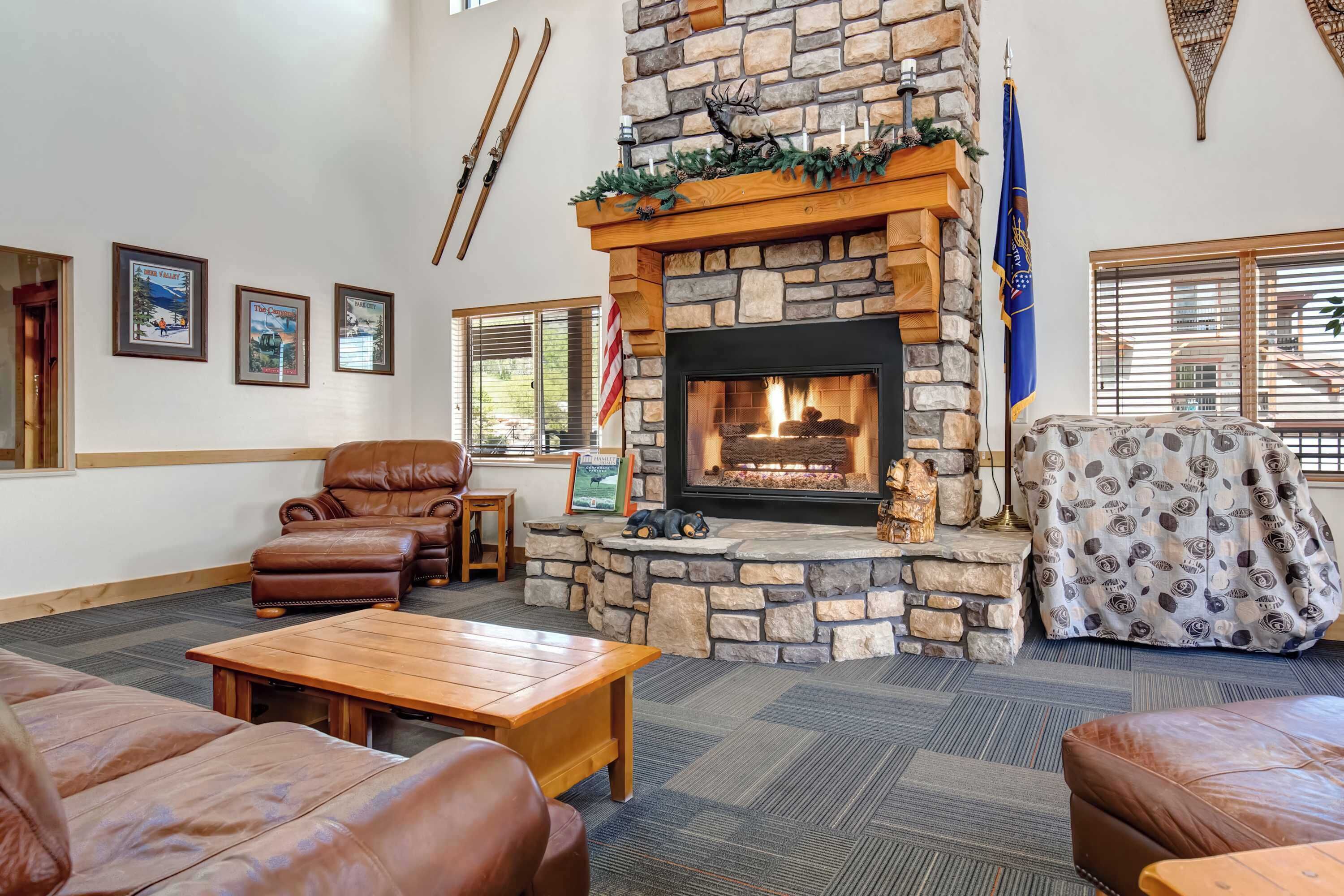 A stone fireplace with a fire, leather sofas, a wooden coffee table, and framed pictures on the wall.