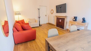 Ein Wohnzimmer mit einer Couch, einem Tisch, einer Lampe, einem Kleiderständer, einem Kamin und einem Fernseher.