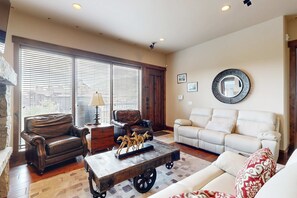 A living room with a brown leather armchair, a white sofa, a wooden coffee table with horse figurines, and a large mirror on the wall. - Sophisticated Mountain-View Condo - Hot Tub, Heated Pool - Walk to Gondola (Park City)