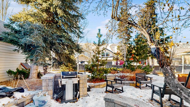 Un patio trasero con una parrilla, asientos de piedra y suelo cubierto de nieve.