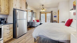 Una habitación con cama, escritorio, refrigerador, armarios de madera y ventilador de techo.