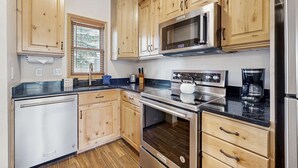 Una cocina con armarios de madera, horno de acero inoxidable, microondas y cafetera.