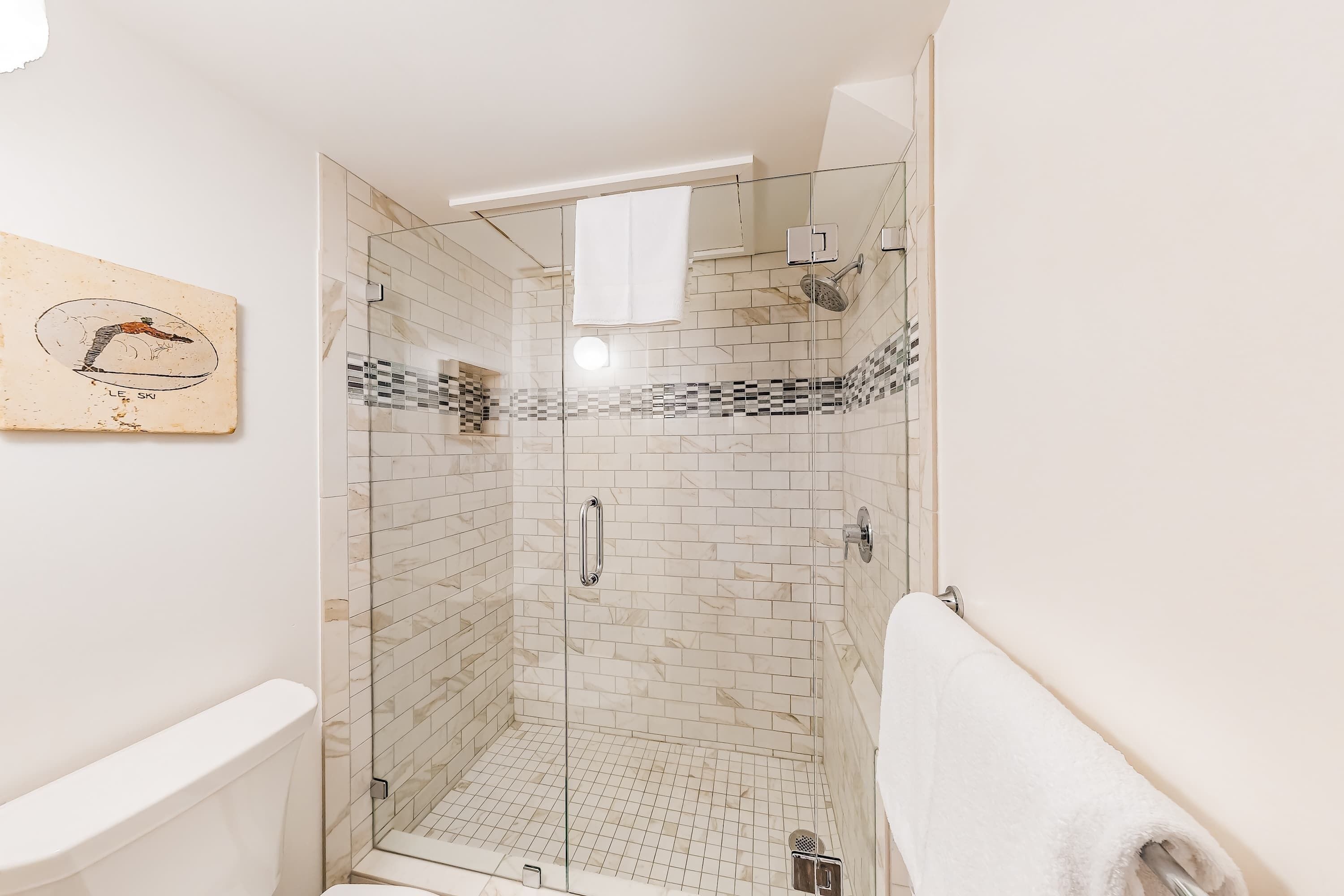 Eine Dusche mit Glastüren, eine weiße Toilette und ein Handtuch an der Wand.