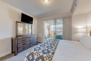 Ein Hotelzimmer mit Bett, Schminktisch, Fernseher, Balkon mit Aussicht und einem fenster mit Vorhängen.