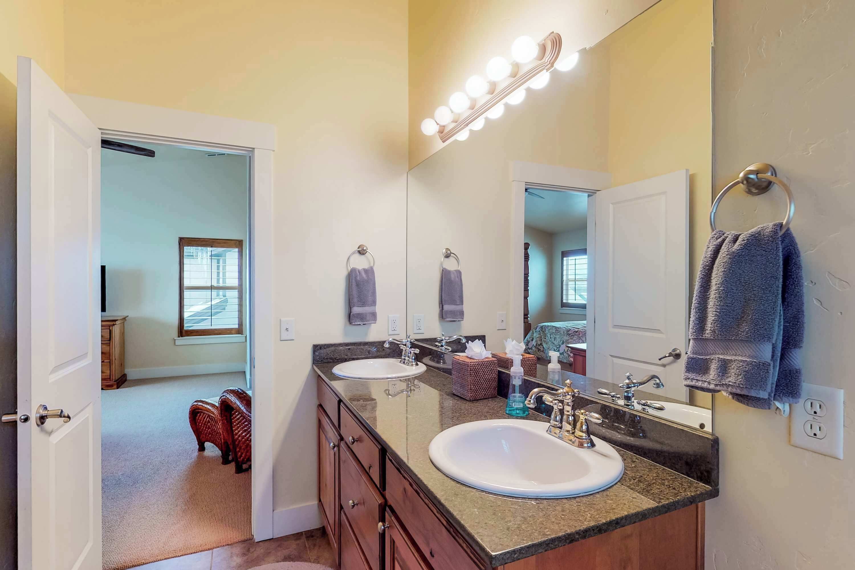 A bathroom with two sinks, a vanity, a mirror with lights, and a towel rack.