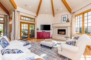 A spacious living room with a fireplace, large windows, and a television.