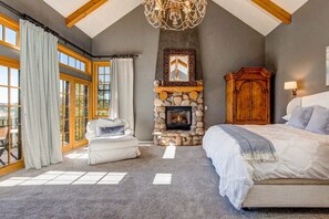 A bedroom with a stone fireplace, a large bed, a white sofa, and a wooden cabinet.