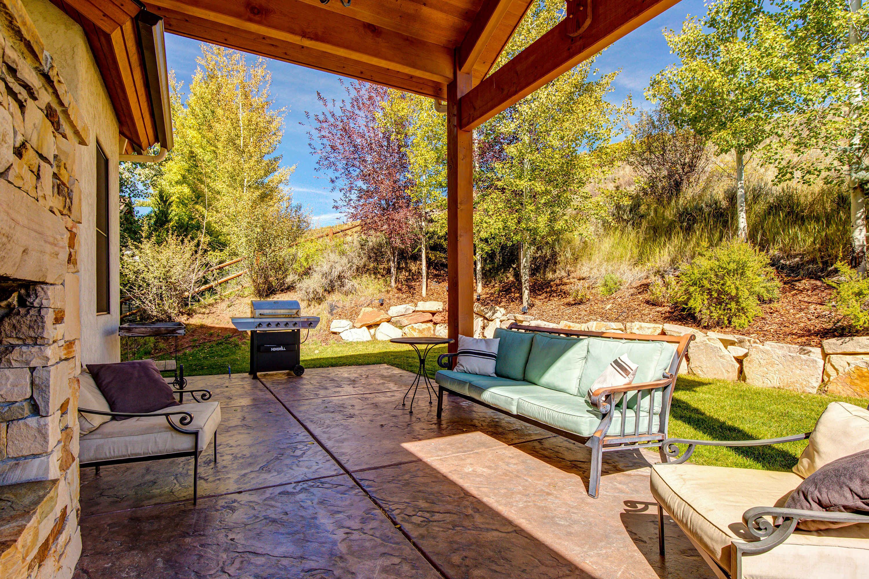 Un patio al aire libre con suelo de piedra, una pérgola de madera, un sofá verde y una parrilla.