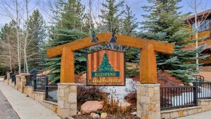 Une arche en bois, surmontée d’une enseigne indiquant le « Redpine Clubhouse », est entourée de murs de pierre et bordée d’un chemin de pierre.
