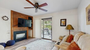 Un salon doté d’une cheminée, d’un ventilateur de plafond, d’un canapé, d’une télévision et offrant une vue à travers une porte vitrée.