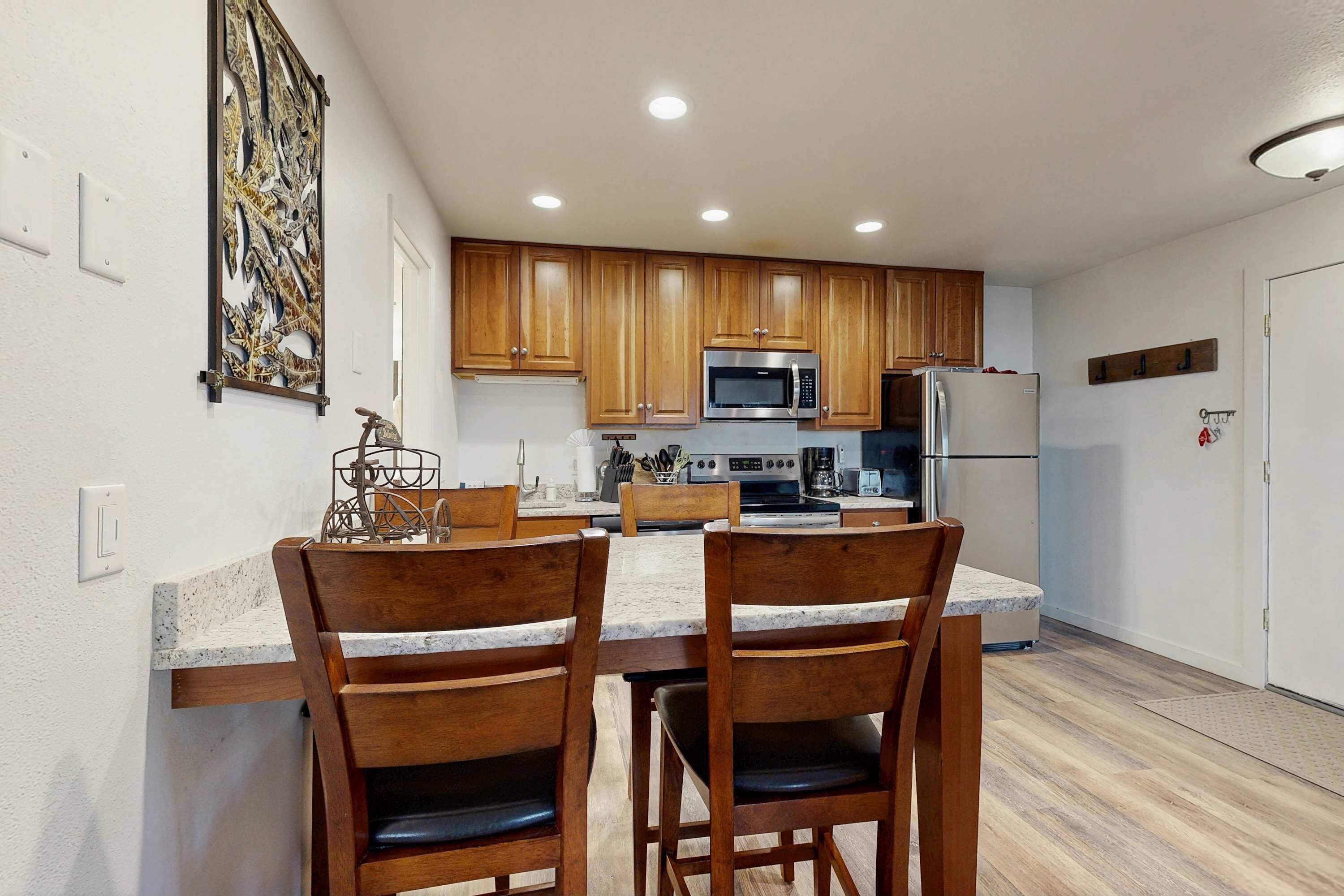 A kitchen with wooden cabinets, a microwave, a refrigerator, and a dining area with two chairs.