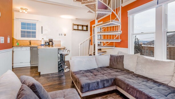 Un intérieur moderne avec un escalier en colimaçon, un canapé, un coin cuisine et une fenêtre offrant une vue agréable.