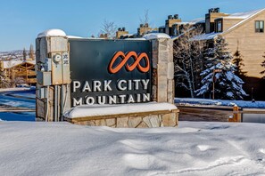 Schild für Park City Mountain mit steinernen Fundament und Metalloberteil, umgeben von Schnee und Gebäuden.