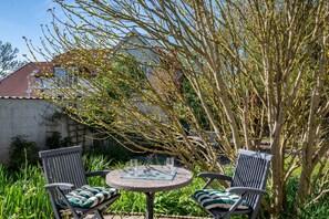 A patio with two chairs and a table, surrounded by greenery and a tree. - Holiday Apartment for 2 Guests (25 m²) in Warnemünde (Baltic Sea Resort) (Rostock)