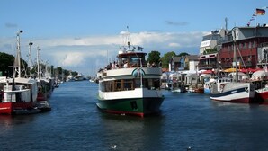 Un puerto con varias embarcaciones amarradas, destacando un barco verde y blanco en el centro, y edificios con balcones a lo largo de la orilla.