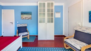 Una habitación con cama, sillón, sofá, armario y un cuadro en la pared.